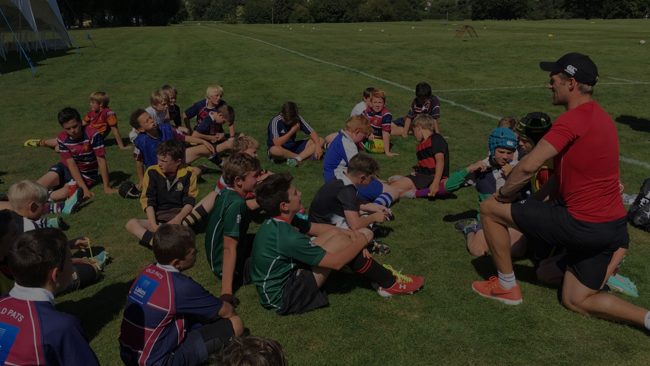 Coach kneeling talking to young rugby players